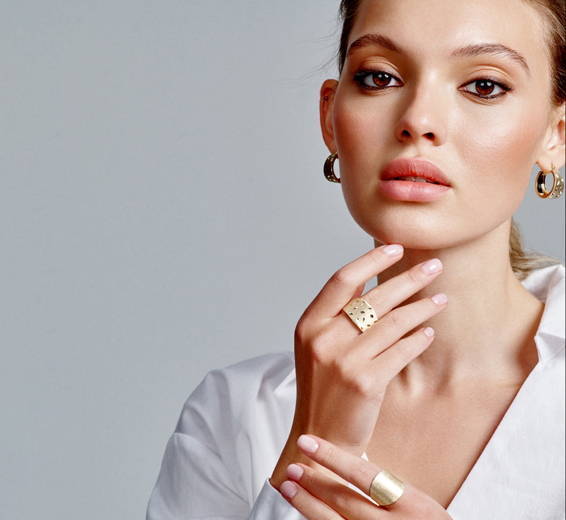 Woman wearing gold jewelry against a gray background