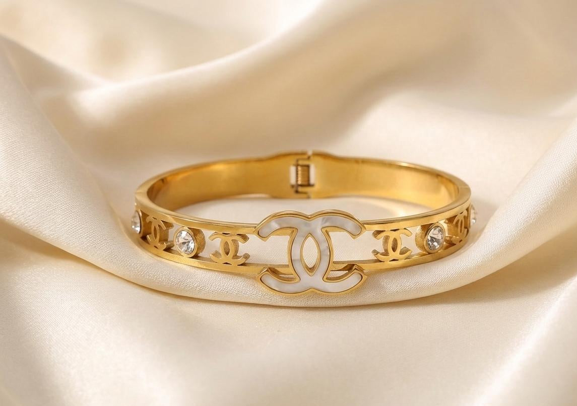 Gold bracelet with Chanel logo on a beige fabric background